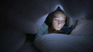 Geceleri bir cep telefonu kullanan küçük kız. bir battaniyenin altında gizleme
