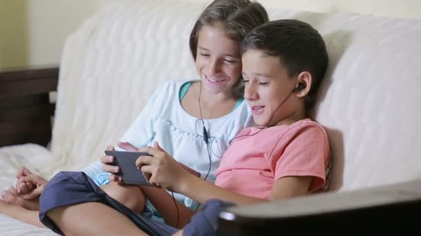 Adolescentes usando smartphone com fones de ouvido. irmão e irmã com um telefone — Vídeo de Stock