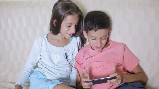 Adolescentes usando smartphone com fones de ouvido. irmão e irmã com um telefone — Vídeo de Stock