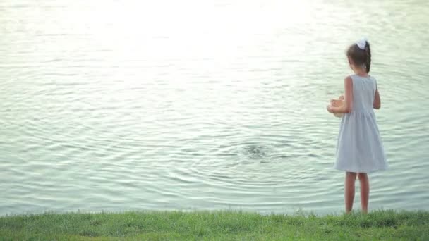 Petite fille en vêtements roses nourrir les poissons dans un étang de jardin. enfant près du lac — Video