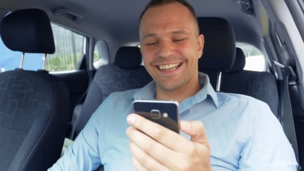 Retrato de um jovem que usa um smartphone enquanto dirige um carro e ri — Vídeo de Stock