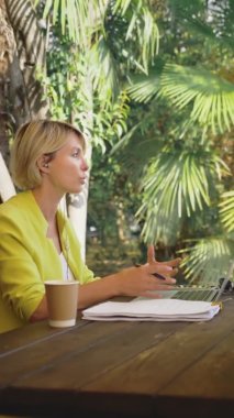 Dikey olarak. İş kadını, açık bir kafede dizüstü bilgisayarla video konferansı düzenliyor.