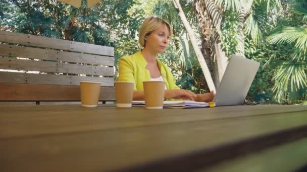 Трудоголичка работает на ноутбуке в кафе на открытом воздухе с тремя чашками кофе — стоковое видео