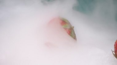 Aşırı yakın plan, detaylı. Kırmızı çilekler dumanın içinde kuru buzun üzerinde yatıyor.