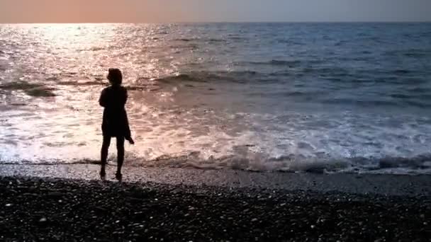 Silhouette d'une femme debout au bord de la mer dans une robe courte flottant dans le vent — Video