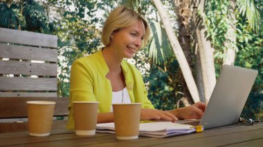 İşkolik bir kadın dışarıda, kafede dizüstü bilgisayarda üç fincan kahveyle çalışıyor.