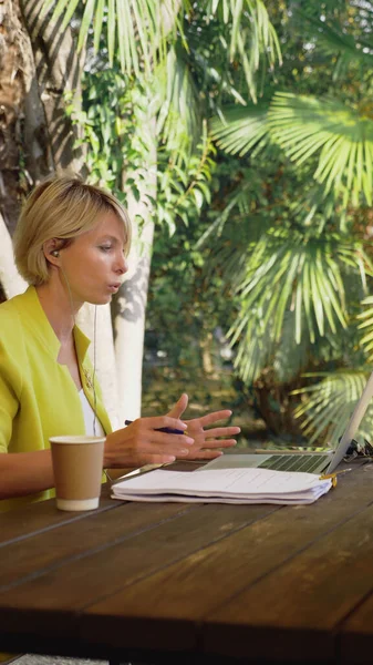 Secara vertikal. pengusaha yang mengadakan konferensi video melalui laptop di sebuah kafe luar ruangan — Stok Foto