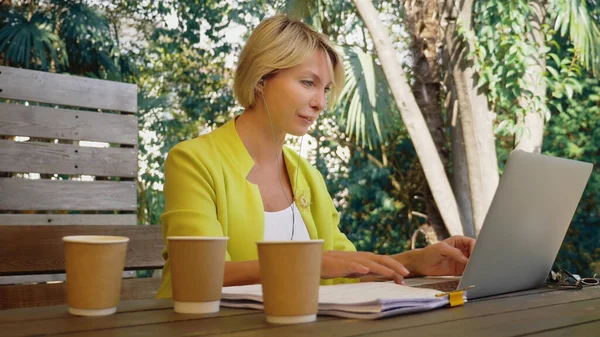 Femme accro au travail travaillant sur ordinateur portable dans un café à l'extérieur avec trois tasses de café — Photo