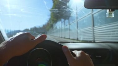 Şehirde araba süren bir adamın birinci şahıs görüntüsü. Güneş parlıyor