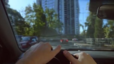 Şehirde araba süren bir adamın birinci şahıs görüntüsü. Güneş parlıyor