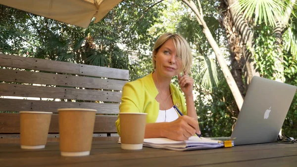 Femme accro au travail travaillant sur ordinateur portable dans un café à l'extérieur avec trois tasses de café — Photo