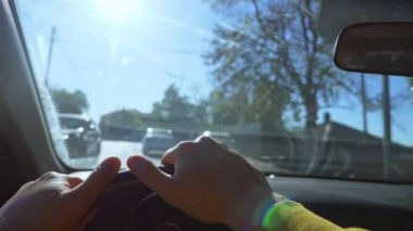Şehirde araba süren bir adamın birinci şahıs görüntüsü. Güneş parlıyor