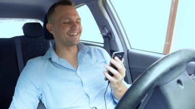 Araba kullanırken akıllı telefon kullanan ve gülen bir gencin portresi.