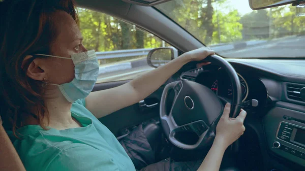 Una mujer en una camiseta y una máscara médica está conduciendo un coche — Foto de Stock
