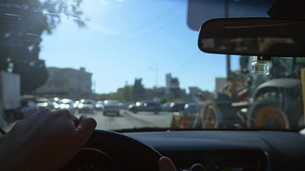Vista in prima persona di un uomo che guida un'auto in movimento per la città. bagliore del sole — Foto Stock