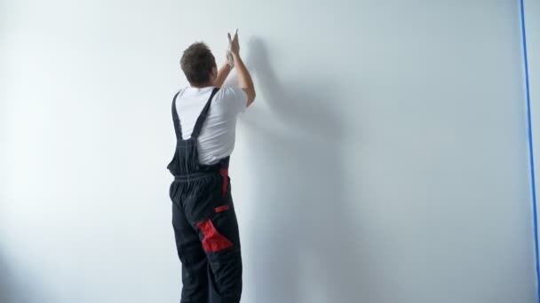 A man in work overalls paints a white wall with white paint with his hands — Stock Video