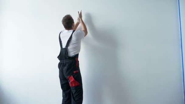 A man in work overalls paints a white wall with white paint with his hands — Stock Footage A man in work overalls paints a white wall with white paint with his hands Video Clip