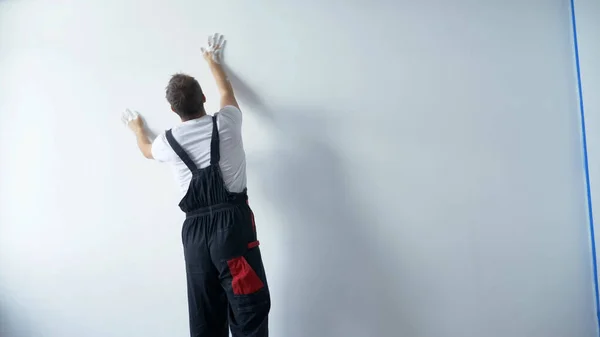 Чоловік у робочому комбінезоні малює білу стіну білою фарбою своїми руками — стокове фото