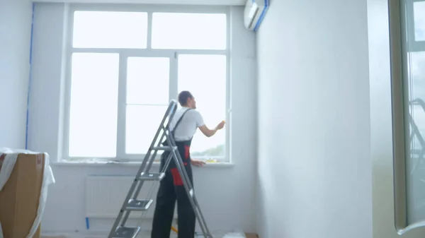 Wazige achtergrond. een man op een trapladder schildert de muren in de kamer wit — Stockfoto