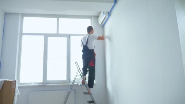 Fondo borroso. un hombre sobre una escalera pinta las paredes de la habitación de blanco — Vídeo de stock
