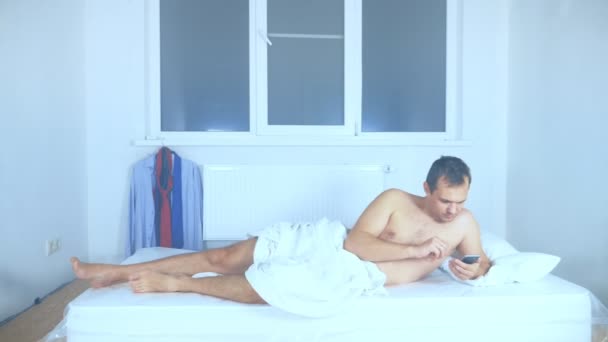 발가벗은 남자가 빈 방에 있는 매트리스에 누워 전화기를 사용하고 있다 — 비디오