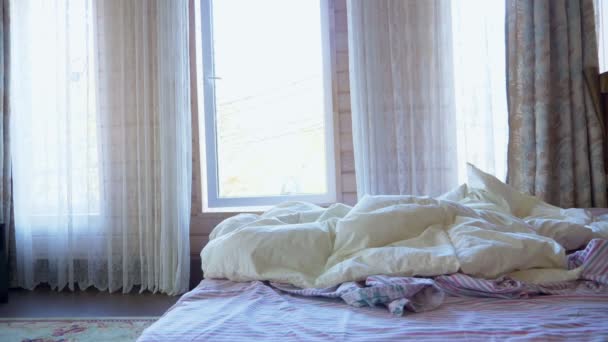 Un hombre cae en la cama en una habitación con grandes ventanales — Vídeo de stock