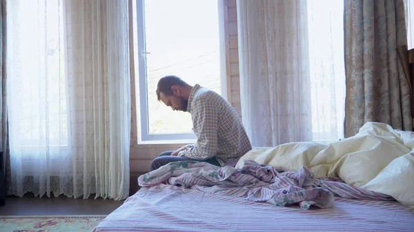 Sleepy man puts on a sock while sitting on the bed — Stock Photo, Image