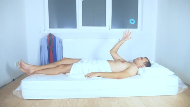 En man ligger på en madrass i ett tomt rum och skämmer bort — Stockvideo