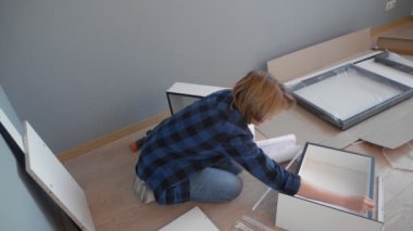 Kadın evde yerde otururken mobilya topluyor.