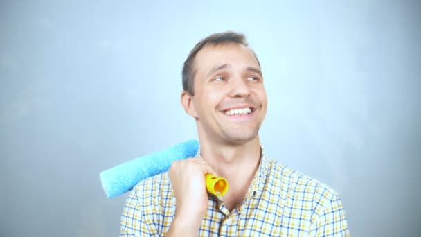 Retrato de un hombre con un rodillo para pintar mirando a la cámara y sonriendo — Vídeos de Stock