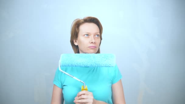 Mujer cansada con un rodillo de pintura sobre un fondo azul. espacio de copia — Vídeos de Stock