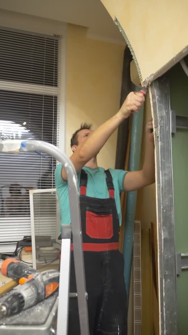 Вертикальная. улучшения дома. мужчина разбирает арку гипсокартона в комнате — стоковое видео
