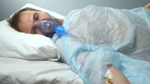 Человек в кислородной маске с капельницей лежит на кровати в больнице — стоковое видео