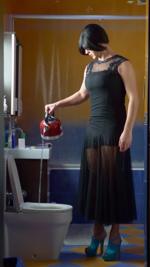 Un homme déguisé en femme versant de l'eau bouillante d'une bouilloire dans les toilettes. — Video