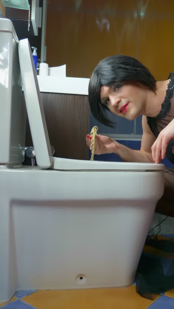 Pionowo. mężczyzna przebrany za kobietę jedzącą makaron z toalety — Wideo stockowe