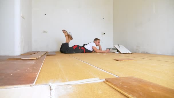 Строитель в отремонтированной комнате лежит на полу с помощью смартфона — стоковое видео