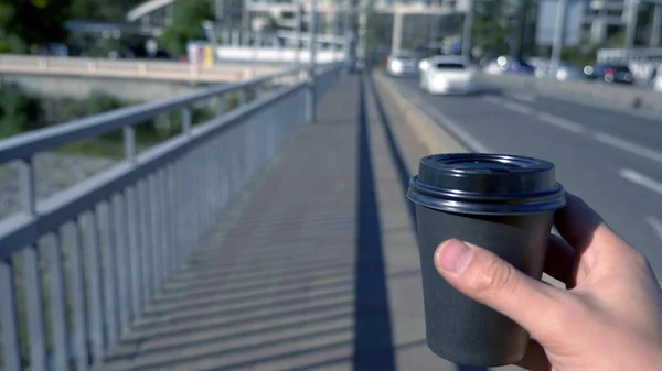 Un hombre sostiene una taza de café desechable en sus manos y camina por la calle — Foto de Stock