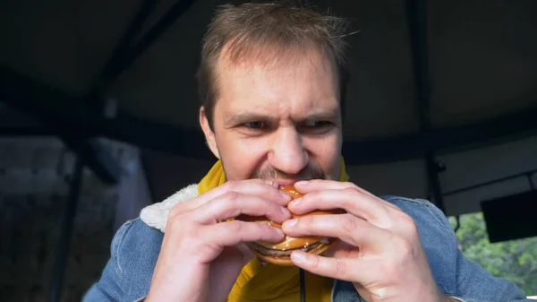 Retrato del hombre enojado comiendo hamburguesa en la cafetería de comida rápida — Foto de Stock