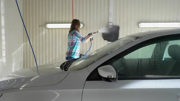 Jovem mulher lava um carro em uma lavagem de carro self-service. — Fotografia de Stock