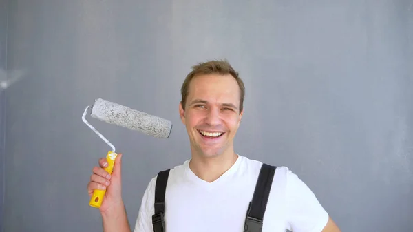 A handsome man in work overalls with a paint roller looking at the camera — Stock Photo, Image