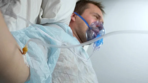 Vertikal. seorang pria dengan masker oksigen dengan dropper terletak di tempat tidur di rumah sakit — Stok Foto