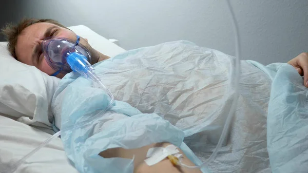垂直。戴着氧气面罩、头戴水滴的男人躺在医院的床上 — 图库照片