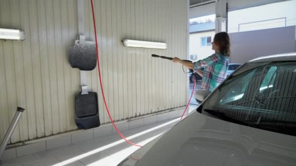 Młoda kobieta myje samochód w samoobsługowej myjni. ogólny plan — Wideo stockowe