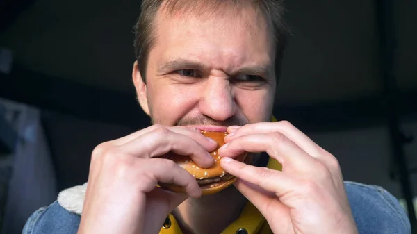 Retrato del hombre enojado comiendo hamburguesa en la cafetería de comida rápida — Foto de Stock