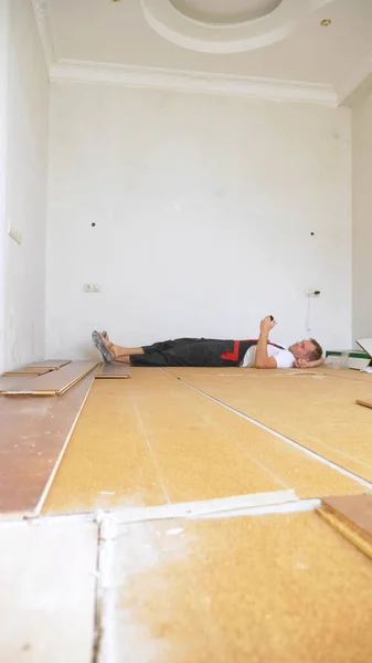 Constructeur dans la chambre rénovée couché sur le sol en utilisant un smartphone — Photo