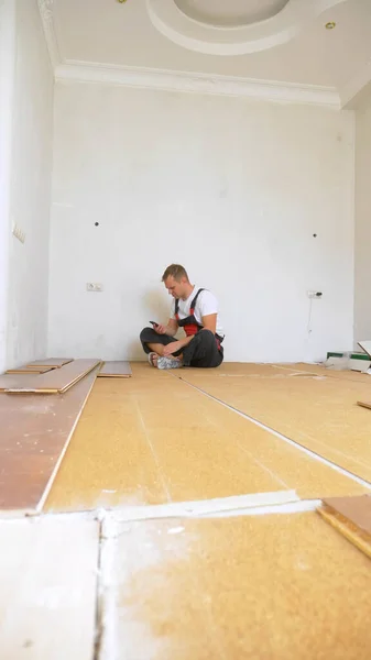 Builder v zrekonstruované místnosti ležící na podlaze pomocí smartphonu — Stock fotografie