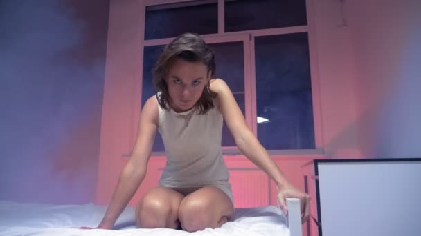 En bedövad kvinna i vit klänning sitter på en säng i ett rökigt rum — Stockvideo