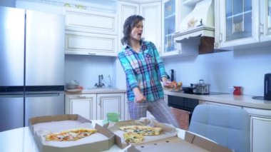 Neşeli Kız evde, mutfakta dans ediyor. Masanın üzerinde bir kutu pizza.