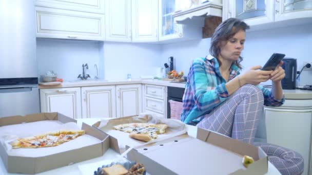 Chica usando el teléfono inteligente mientras se sienta en casa en su cocina — Vídeos de Stock