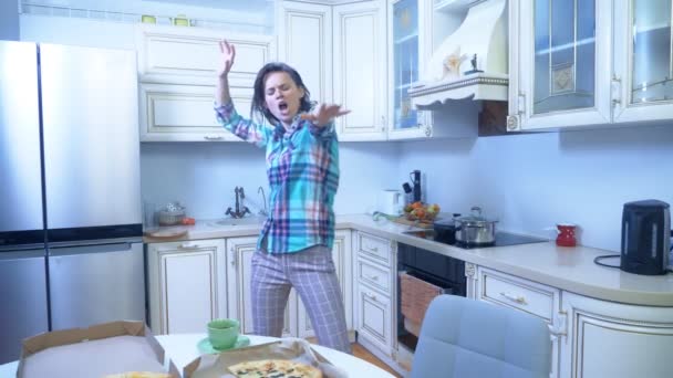 Chica alegre está bailando en casa en la cocina. una caja de pizza sobre la mesa — Vídeos de Stock